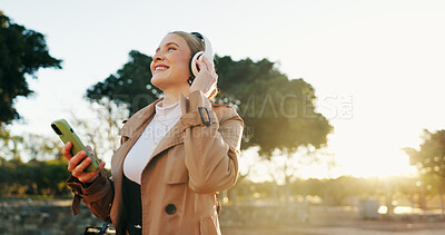Woman, business and headphones with cellphone in park for work commute, streaming or podcast. Female person, walking and happiness in urban city for morning travel with music, entertainment or audio