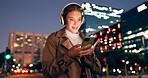 Woman, outdoor and smile on smartphone with headphone for music playlist, entertainment at night in New York. Female person, happy and internet for streaming platform with song or album and video