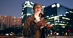 Woman, outdoor and smile on smartphone with headphone for music playlist, entertainment at night in New York. Female person, happy and internet for streaming platform with song or album and video