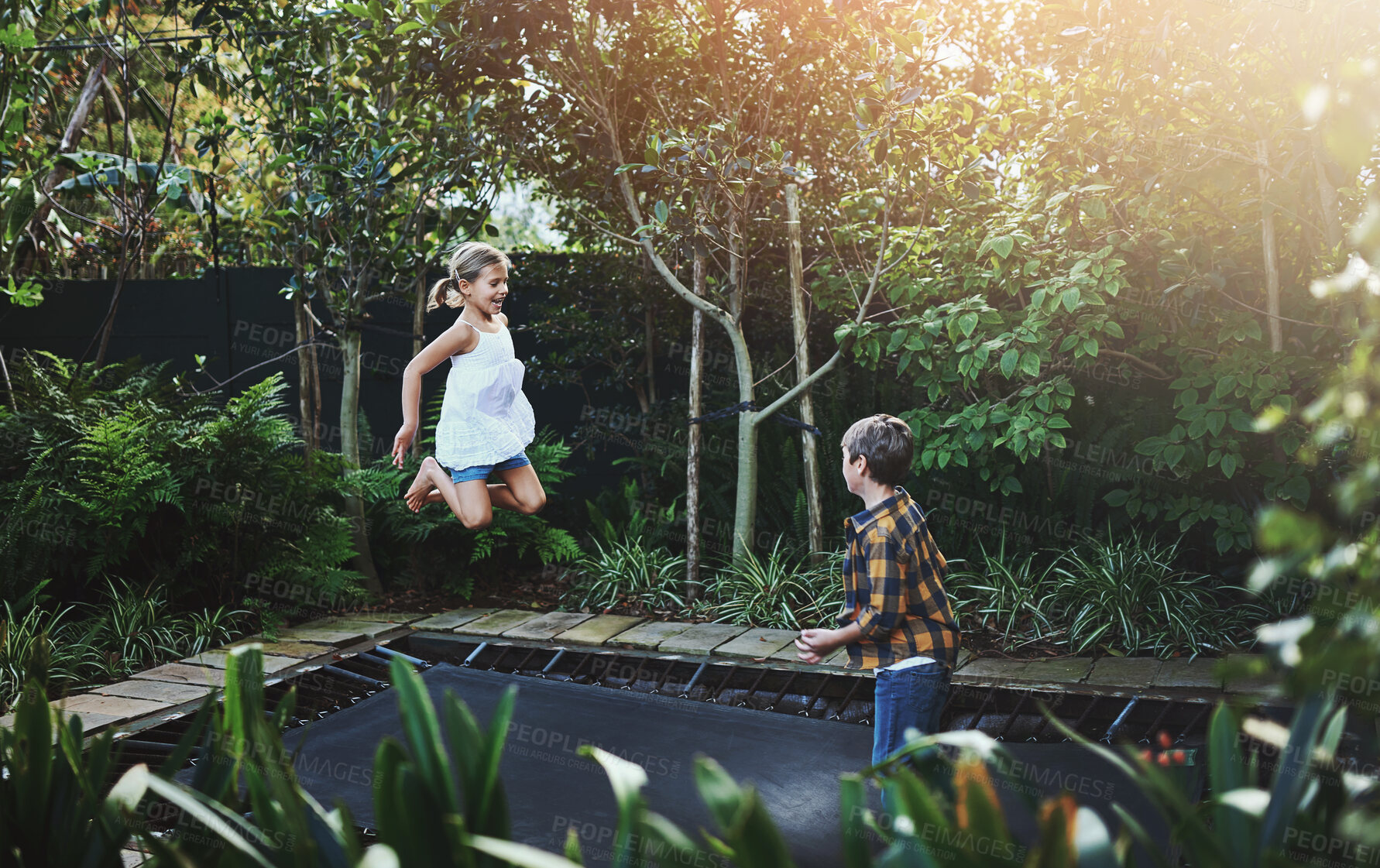 Buy stock photo Nature, jumping and children on trampoline in backyard for fun, hobby or activity together. Happy, energy and kids bounce on rebound tumbler for bonding and playing in outdoor garden with trees.