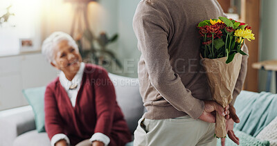 Old man, woman and surprise of flower bouquet on couch, happy and couple in living room of house. Senior, male person and partner with gift for love, smile and happiness in home and retirement