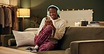 African woman, headphones and phone on sofa with smile, laugh and excited for music in home living room. Girl, smartphone and happy for streaming, audio subscription and mobile app on couch in house