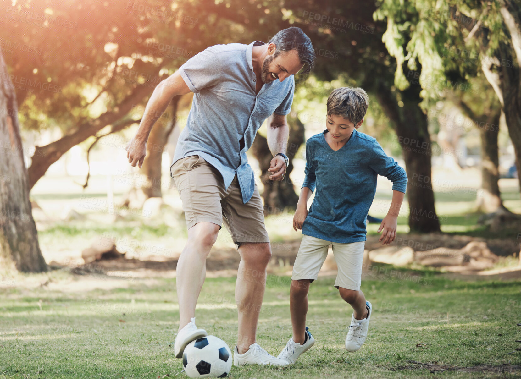 Buy stock photo Nature, football and father playing with child in outdoor park practicing for sports game together. Fun, bonding and dad kicking soccer ball with boy kid for training in field or garden in Canada.