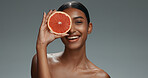 Woman, face and skincare with grapefruit, studio or shine with health, wellness or beauty by dark background. Girl, model and cosmetics with fruit, nutrition or glow with facial aesthetic in portrait