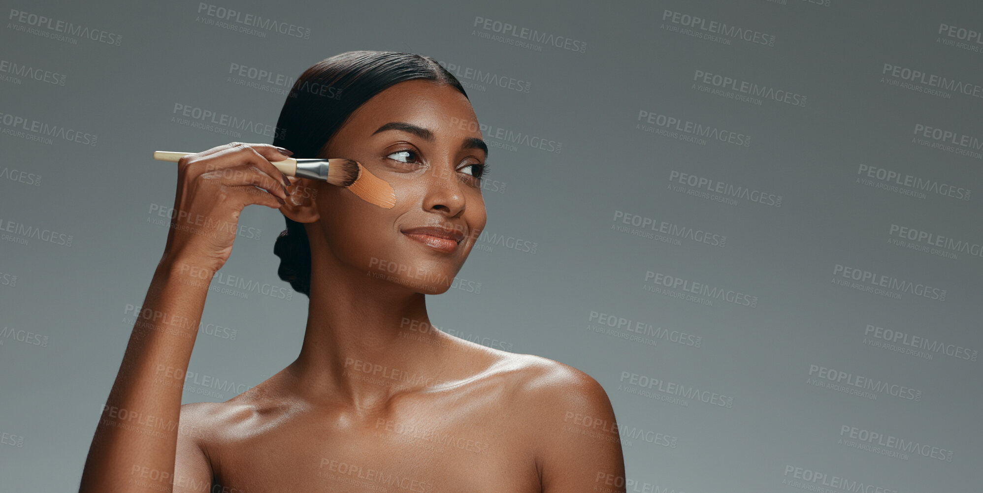 Buy stock photo Beauty, makeup and foundation brush of a woman with cosmetics, smile and dermatology. Portrait of a happy Indian model person with facial care, skin glow and wellness on a grey background in studio