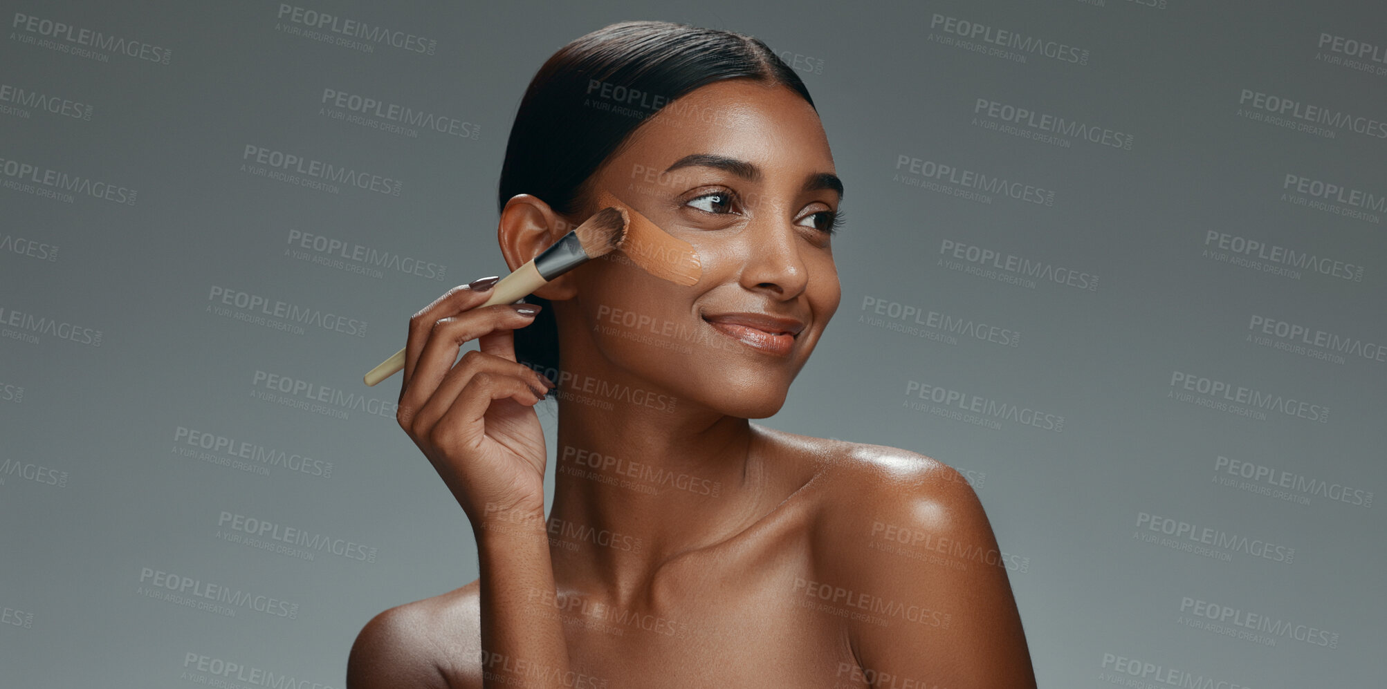 Buy stock photo Beauty, makeup and foundation brush of a woman with cosmetics, smile and dermatology. Portrait of a happy Indian model person with facial care, skin glow and wellness on a grey background in studio