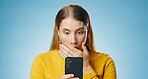 Woman, shocked and reading with smartphone in studio, blog update and message notification on networking app. Social media, communication and promo for news or gossip, blue background and online