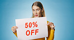 Poster, sale and portrait of woman in studio for news, announcement and information. Shopping, advertising and happy person with sign for half price discount, deal and bargain on blue background