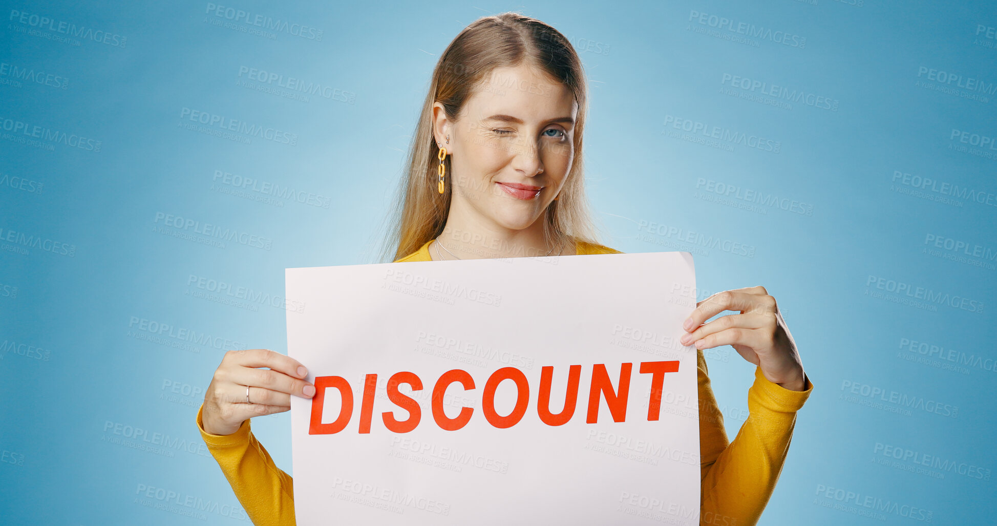 Buy stock photo Woman, wink and discount poster in studio for shopping, retail or sale announcement of store or shop. Young person or seller in portrait with sign, offer and news for makeup deal on blue background