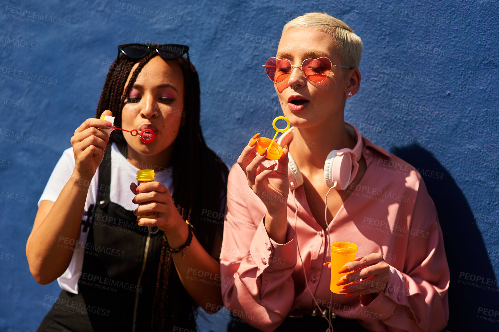 Buy stock photo Young, women or blowing bubbles on wall for fashion or wellness, cool with heart sunglasses and together. Female people, outdoor or backdrop with sunshine, headphones and clothes for style in USA