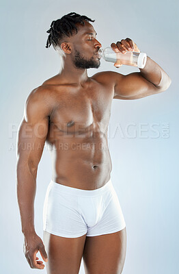 Buy stock photo Black man, drinking and water with underwear in studio for hydration, detox or topless with healthy body. Bodybuilder, person or fitness model with liquid for thirst or wellness on blue background