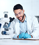 One handsome young mixed race man wearing gloves and a labcoat and looking at medical samples on a microscope in a lab. A male scientist wearing safety goggles and smiling while writing in a notebook 