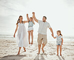 Happy caucasian family of four having fun while enjoying a summer vacation together at the beach shore. Loving parents swinging their cute kids while walking on sand. Bonding and sharing quality time