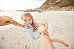 Happy caucasian girl swinging and spinning in circles by the arms at the beach with her father. Cute playful kid having fun while bonding with a parent on a summer vacation outdoors