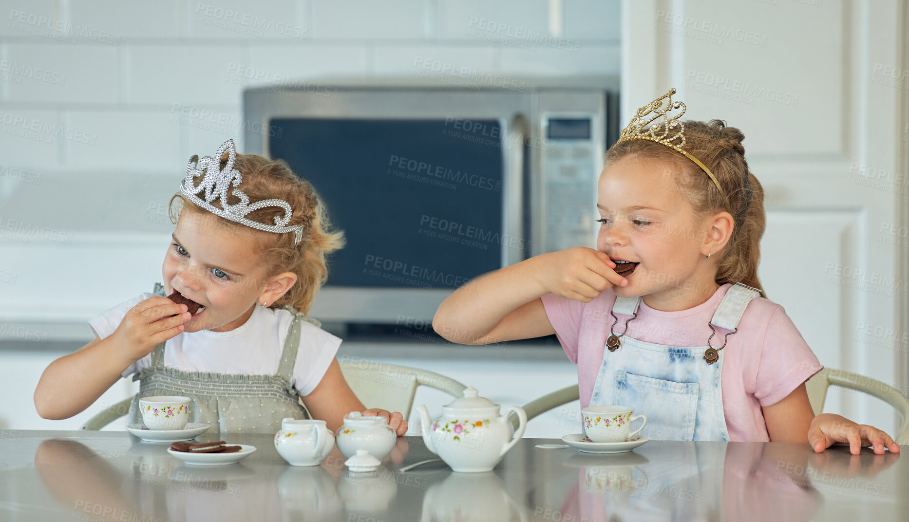 Buy stock photo Girl, children and eating cookies for tea party in kitchen, childhood fun and tiara for pretend playing. Kids, siblings and toys in home with happiness or love, bonding and growth or development.