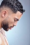 Young mixed race man standing in the shower with water running down his body during his morning grooming routine. Serious hispanic guy rinsing his body with a warm shower practicing good hygiene