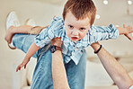 Adorable little caucasian boy lift into the air by his father so he can pretend to fly like a plane or superhero with arms out while relaxing at home. Loving dad playing and bonding with carefree kid