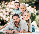 Carefree caucasian family with two kids having fun outdoors. Adorable little girl and boy lying on top of their parents enjoying time at the park. Loving parents bonding with their son and daughter