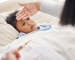 Sick little boy lying in bed while mother takes his temperature with thermometer and feeling forehead. Mother taking care of child with fever