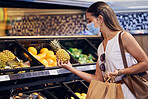 Shopping, checking and holding a fruit with a female checking if its good, ripe and healthy to eat. Young woman with a mask buying fresh and organic food at a retail store or supermarket indoors