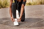 One african american female athlete tying her laces before starting her outdoor workout. A dedicated black woman listening to music and preparing for a run outside. Health and fitness is her lifestyle