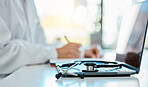 Closeup of a stethoscope lying on a laptop on a desk while a doctor writes a prescription in the background. Medical professional writing notes, planning with a laptop and stethoscope in the office