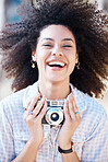 Young mixed race woman with curly hair taking creative photos on a vintage retro film camera. One female photographer looking in viewfinder while capturing pictures as a hobby or profession on a shoot