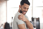 One young hispanic man holding his sore shoulder while exercising in a gym. Guy suffering with painful arm injury from fractured joint and inflamed muscles during workout. Struggling with stiff body cramps causing discomfort and strain
