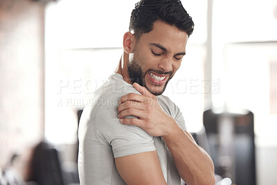 Buy stock photo One young hispanic man holding his sore shoulder while exercising in a gym. Guy suffering with painful arm injury from fractured joint and inflamed muscles during workout. Struggling with stiff body cramps causing discomfort and strain