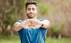 Portrait of one fit young indian man stretching arms for warmup to prevent injury while exercising outdoors. Male athlete preparing body and muscles for training workout or run at the park