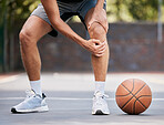 Pain, basketball and man with knee injury standing on outdoor court, holding leg. Sports, fitness and athlete with joint pain, injured and hurt in training, workout and game on basketball court