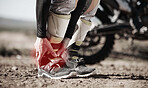 Ankle, injury and motorcycle with the hands of a man holding his joint in pain while outdoor for a race. Sports, training or anatomy with a male athlete suffering an accident on a ride for recreation