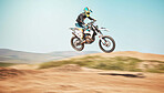 Motorcycle, offroad driving and air jump in desert, blue sky and freedom. Driver, cycling and power stunt on dirt track, competition and motorbike performance on adventure course for fast action show