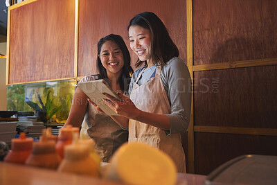 Buy stock photo Cafe, tablet and asian women together at counter checking sales, booking or menu for small business. Social media, content marketing and startup restaurant owner with waitress scroll on digital app.