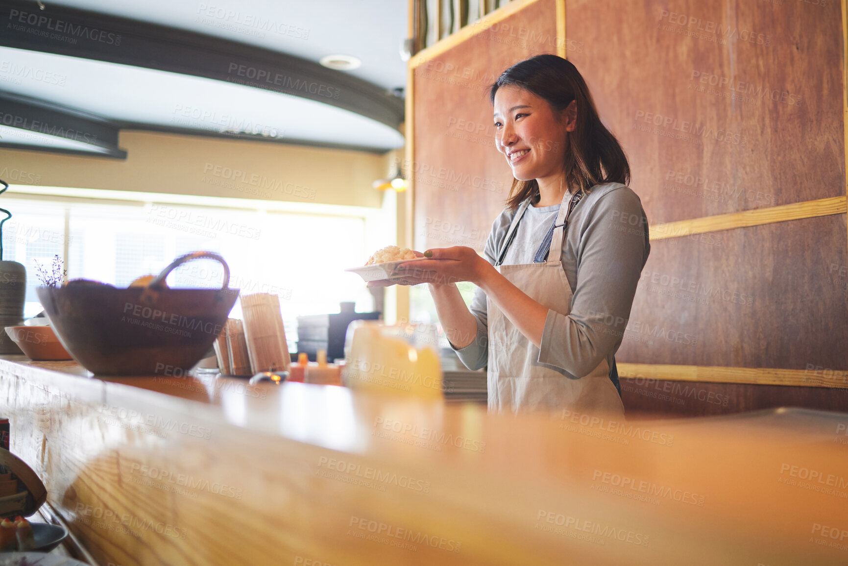 Buy stock photo Chinese food, waitress and an asian woman in a sushi restaurant to serve a traditional meal for nutrition. Kitchen, smile and cooking with a happy young employee in an eatery for fine dining cuisine