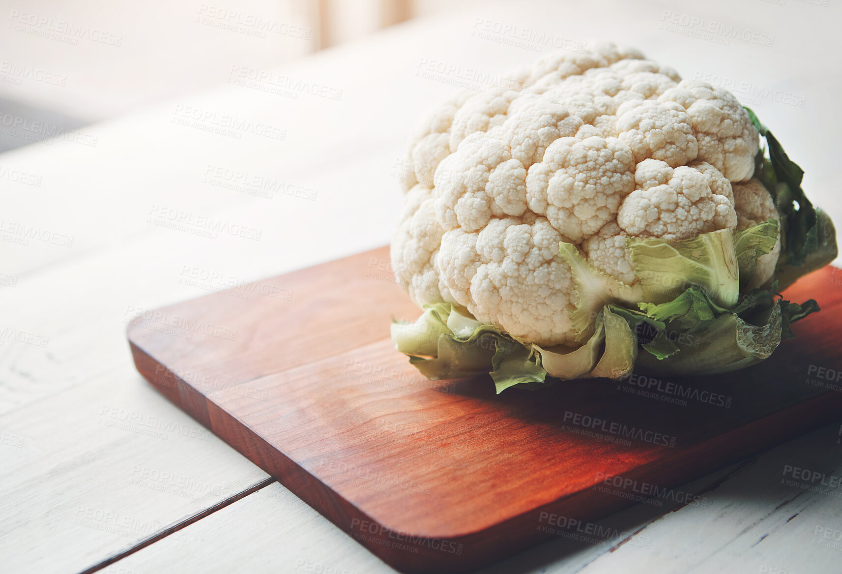 Buy stock photo Cauliflower, wooden board and food in home for health, lunch and choice with nutrition for wellness. Organic vegetable, cooking and chopping block on kitchen table, leaves or meal prep for vegan diet