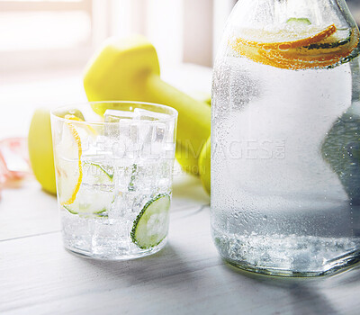 Buy stock photo Cucumber, lemon and water in glass with dumbbell on table for vitamin C, nutrition and organic hydration. Citrus, fitness and ice with liquid in clear jug for antioxidants, detox and healthy drink