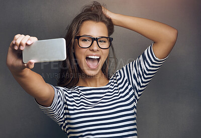 Buy stock photo Selfie, smile and woman with glasses, picture and happiness with social media on grey studio background. Person, human and model with smartphone, connection and memory with reaction and expression