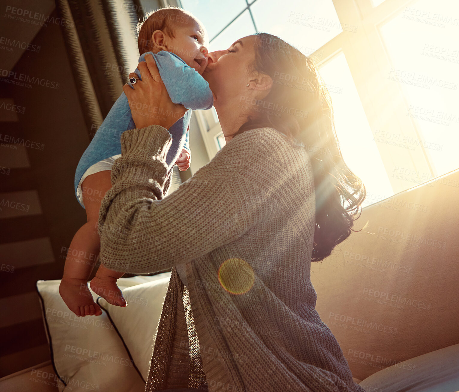 Buy stock photo Mother, baby and kiss on sofa in living room with love for relationship with new born, care and embrace. Light, sunshine and relax with bonding on couch, happiness and playing with child in home.