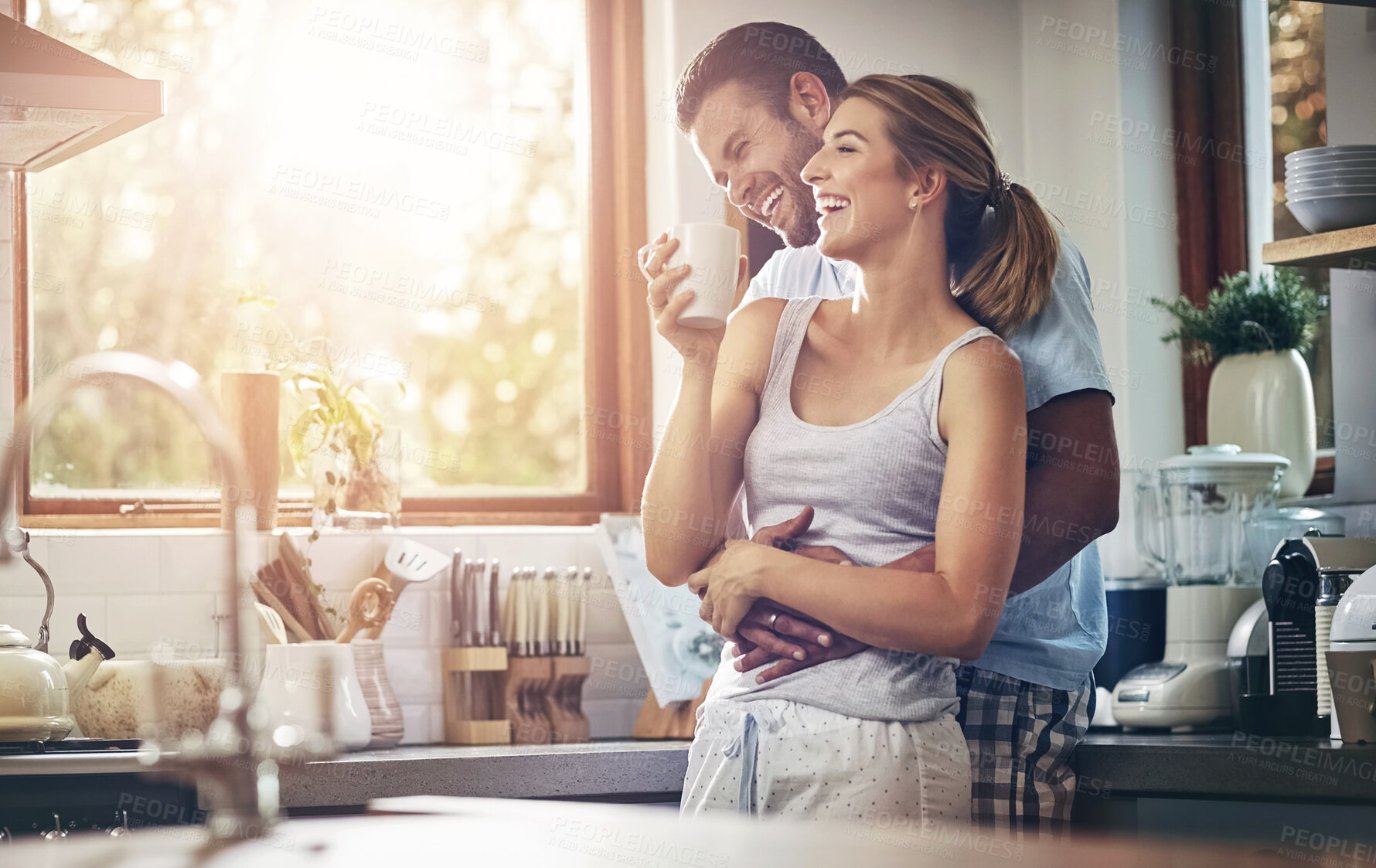 Buy stock photo Coffee, hug and laughing with couple in kitchen of home together for morning break or wellness. Funny, smile or tea with happy man and woman drinking fresh beverage in apartment for love or romance