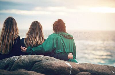 Buy stock photo Friends, beach and sunset of people sitting on rock for bonding, back view and embrace in Ireland. Vacation, group and relax for fun day by ocean, nature or contemplation in outdoors for togetherness