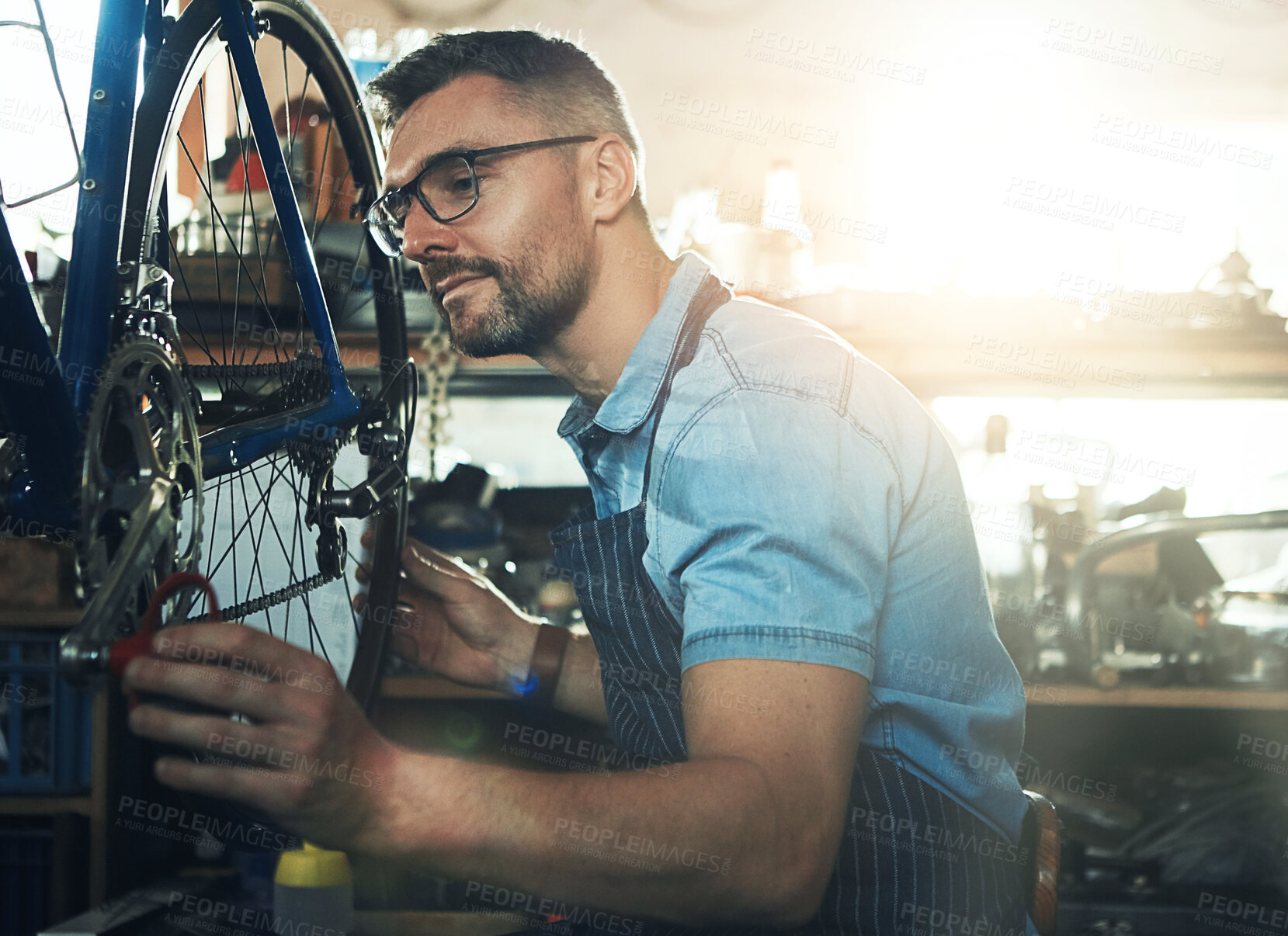 Buy stock photo Bicycle technician, working and repair in shop with frame, chain and tools for maintenance or cycling. Man, bike and mechanic in workshop as handyman for gear, inspection and safety with glasses