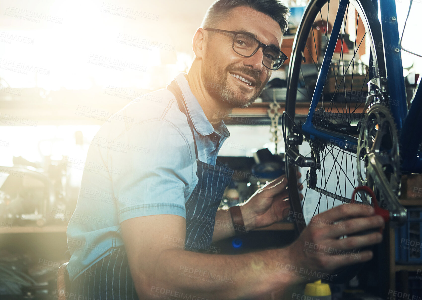 Buy stock photo Man, garage and happy as bicycle mechanic with lens flare in startup or small business.  Workshop, portrait and smile  or confident as handyman with fixing bike at repair or maintenance shop
