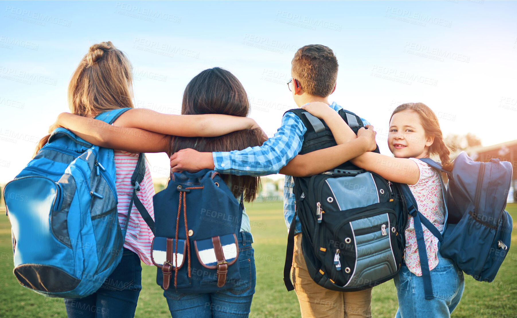 Buy stock photo School kids, group and back with hug, outdoor and together with support, solidarity and development. Children, girl and portrait for learning, education and future with backpack on lawn at academy