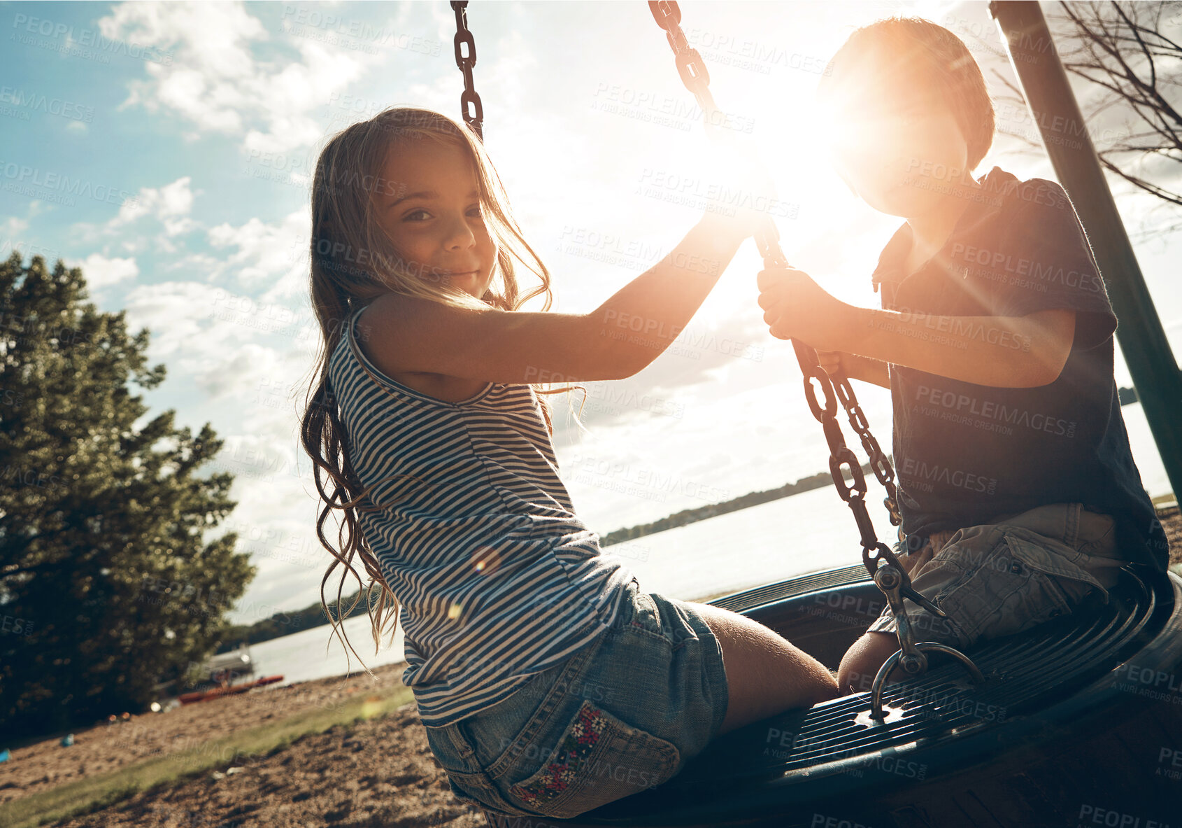 Buy stock photo Children, tyre swing and play in outdoor, bonding and friends at playground for game or adventure. Kids, lens flare and together for fun in backyard or freedom, siblings and connection on vacation