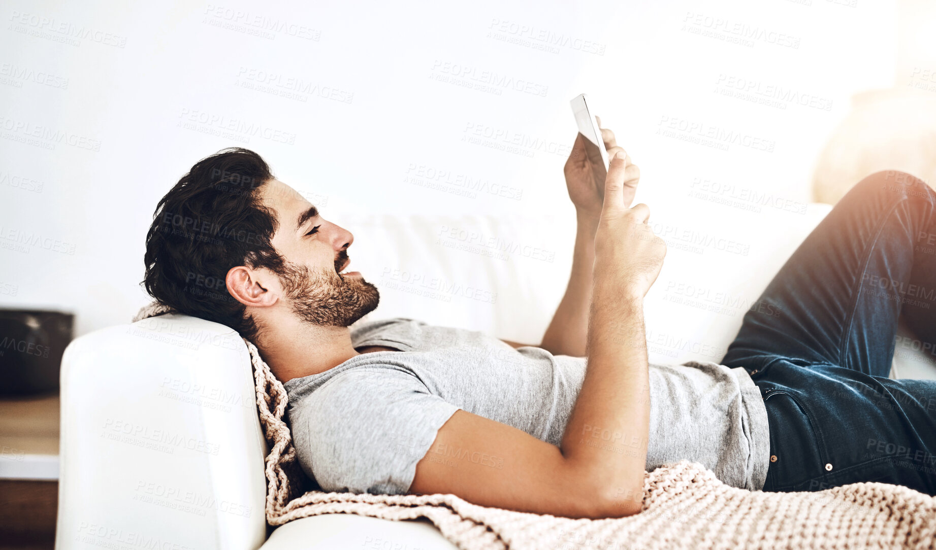 Buy stock photo App, relax and tablet with man on sofa in living room of home for streaming or weekend time off. Break, social media and technology with happy person lying on couch in apartment for rest or wellness