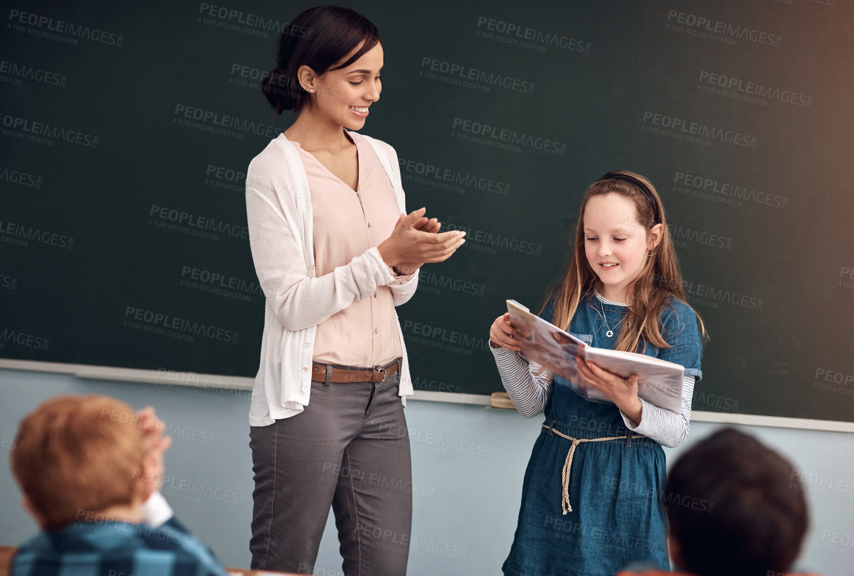 Buy stock photo Reading, book and girl in classroom, teacher and clapping for student, smile and learning of literature. Proud, woman and applause in school, growth or development of children, knowledge or education