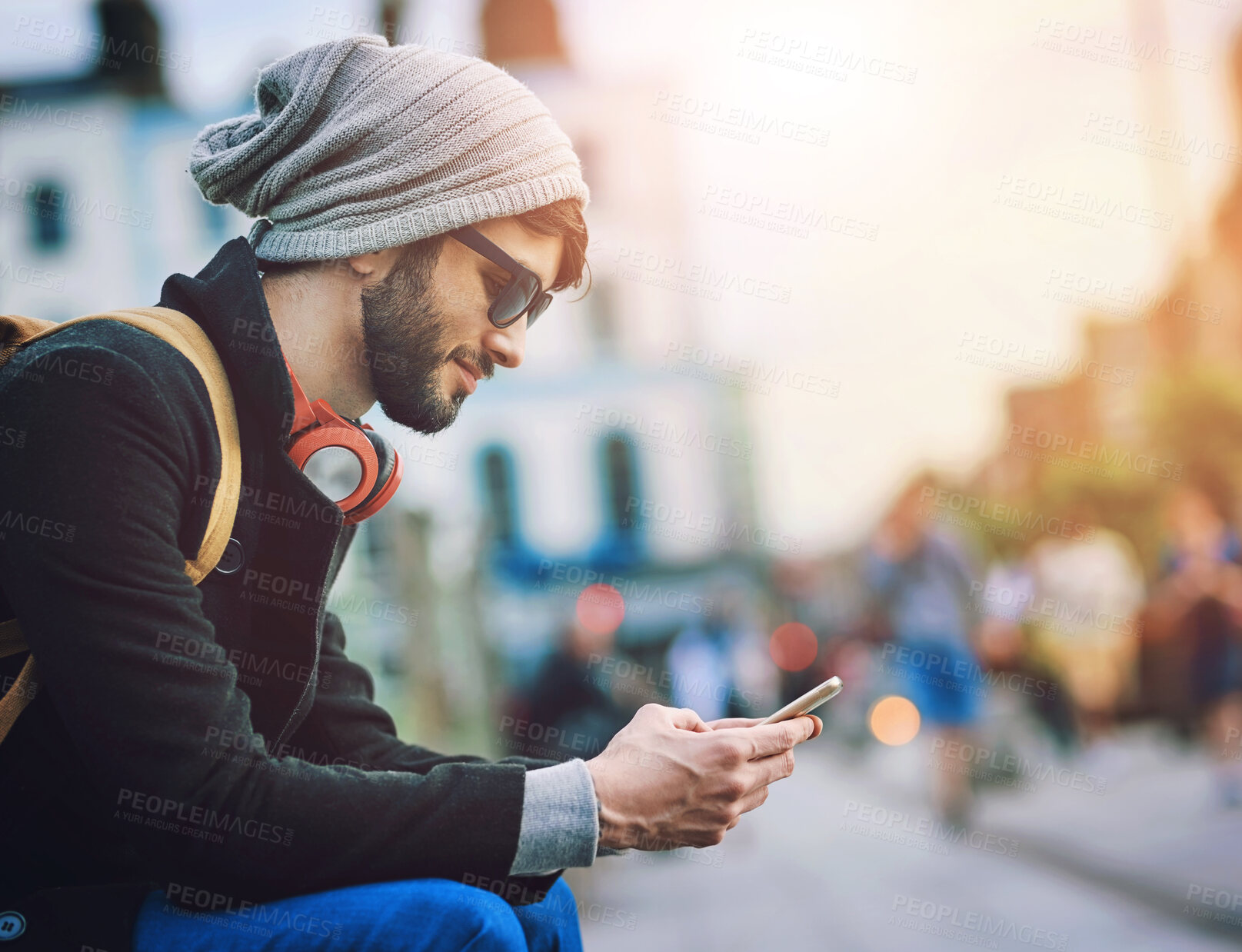 Buy stock photo Man, smile and phone on bench in city, communication and social media to commute for sightseeing location. Male person, travel and headphones on mobile, station and texting for transport schedule
