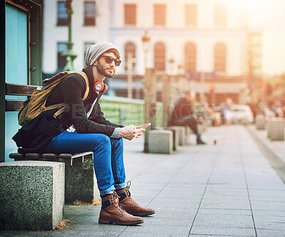 Buy stock photo Man, travel and phone on bench in city, commute and waiting on bus for thinking of sightseeing or location. Male person, fashion and headphones on mobile, station and bus stop for transport journey