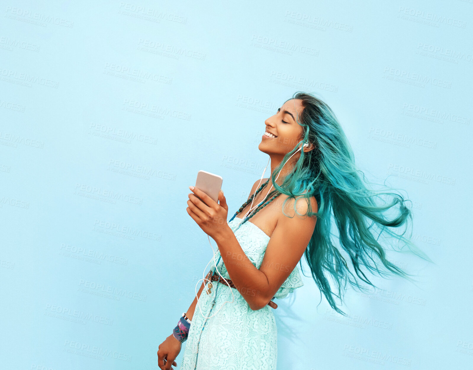 Buy stock photo Happy woman, dance and music in studio with fun, expression and online for streaming on blue background. Hair, earphones and gen z girl with movement for freedom, energy or listening to favorite song